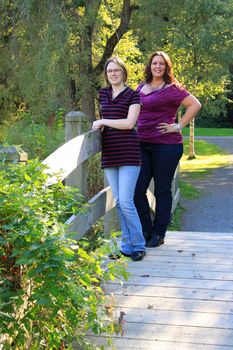 Attractive mother and daughter family standing on a wooden bridge in the outdoors