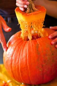 A child's hand lifts the top of a pumpkin after carving it out at a fall festival for Halloween.