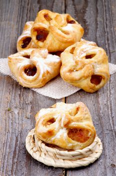 Arrangement of Homemade Pastry Baskets Jam Wrapped with Sugar Powder on Wicker Napkin and Plate closeup on Rustic Wooden background. 