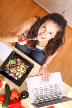 Online information for vegetarians. A young girl eating salad while using a Laptop.