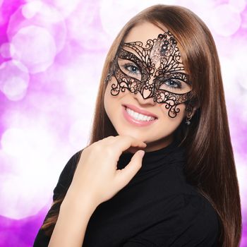 Beautiful woman in carnival mask over pink bokeh background