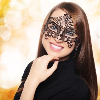 Beautiful woman in carnival mask over golden bokeh background