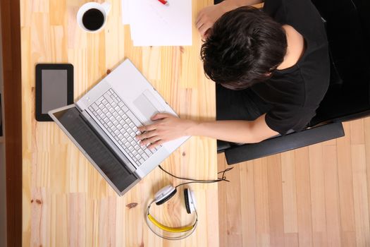 A young hispanic man working on a wooden desk with a laptop.