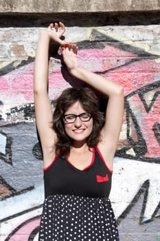 A vintage style dressed girl leaning at a graffiti wall and enjoying the sunlight.