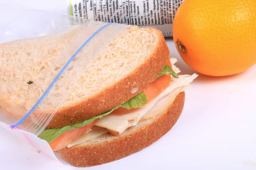 Turkey and cheese sandwich on whole wheat bread with tomato and lettuce inside a zipped bag ready for lunch and orange on the side