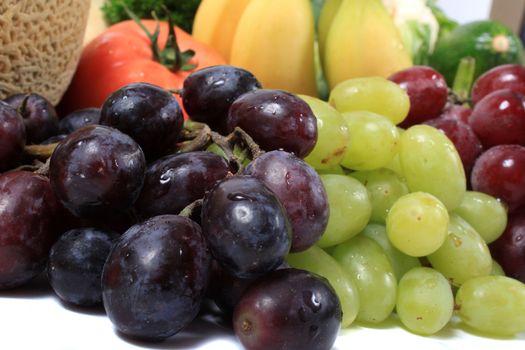 Three different types of grapes in red, green and black along with other healthy vegetables and fruits like bananas and tomatoes