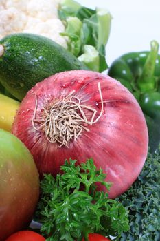 Healthy red or spanish onion in the middle of green vegetables such as kale, peppers, zuchini, parsley and cauliflower