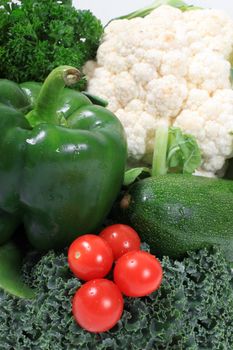 Colorful red cherry or grape tomatoes surrounded by green vegetables such as kale, peppers and zucchini