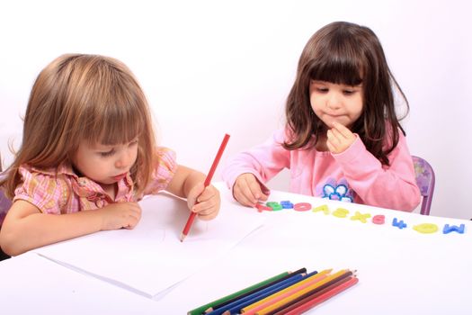 Two little preschool girls, one drawing with pencil the other playing with letters