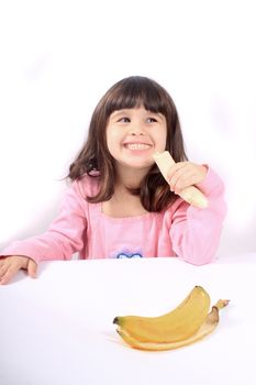 Young little girl making a funny face eating a healthy banana