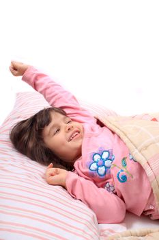 Cute little girl stretching her arms happily with a smile from waking up in her bed.