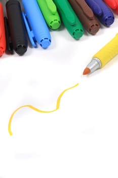Colorful rainbow markers in blue, green,  and reds on a white background with yellow scribble and pen in the foreground