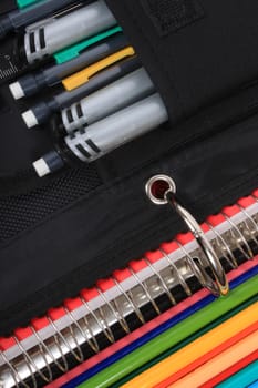 Close up abstract of colorful sharpened  pencil crayons for school  beside  three ring binder containing pens and pencils in pocket