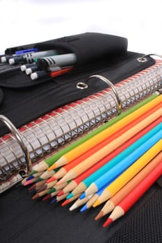 Colorful sharpened  pencil crayons for school  beside  three ring binder containing pens and pencils in pocket