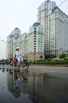 HO CHI MINH, VIET NAM- DEC 15: People ride bicycle on street with high-class high-rise building background, the building reflect on surface water on street  in Ho Chi Minh, Viet Nam on Dec 20, 2013