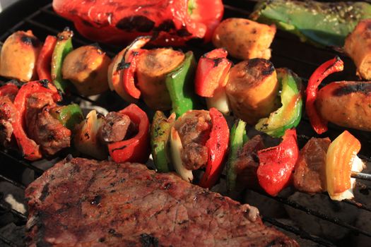 Barbecuing shish kabobs with sausage, steak and peppers, in green and red on a portable charcoal bbq
