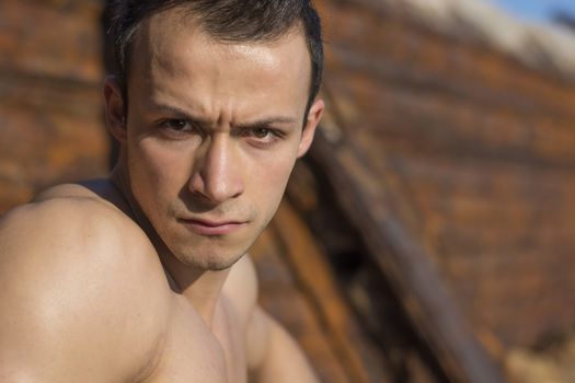 Young man with stern severe eyes looking directly in camera. Outdoors shot
