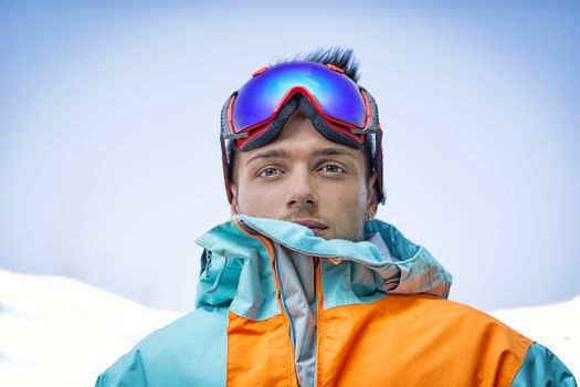 Friendly attractive skier or snowboarder against blue sky looking at camera