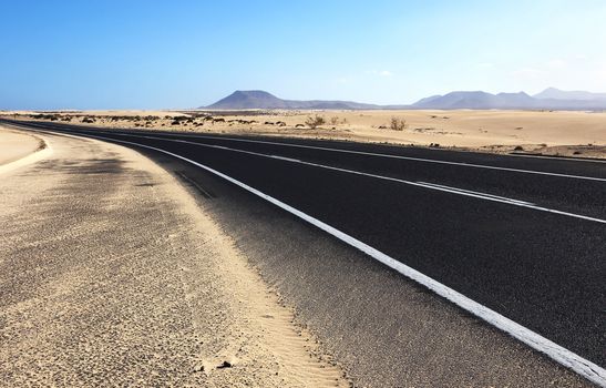 Winding road through the dunes of Corralejo with volcano in the background, in Fuerteventura, Canary Islands, Spain.