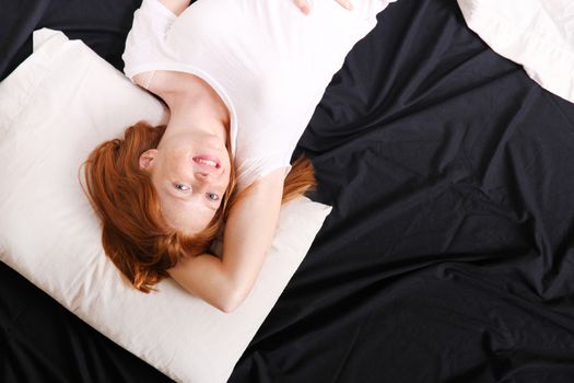 A young adult Woman lying on bed, smiling.
