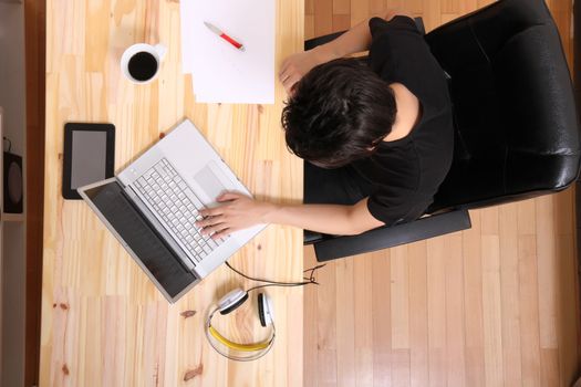 A young hispanic man working on a wooden desk with a laptop.