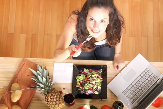 Online information for vegetarians. A young girl eating salad while using a Laptop.