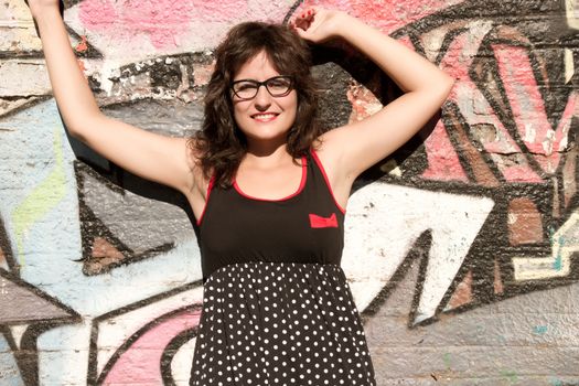 A vintage style dressed girl leaning at a graffiti wall and enjoying the sunlight.