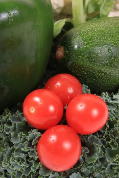 Colorful red cherry or grape tomatoes surrounded by green vegetables such as kale, peppers and zucchini