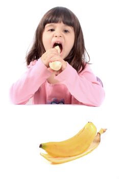 Young little girl making a funny face eating a healthy banana