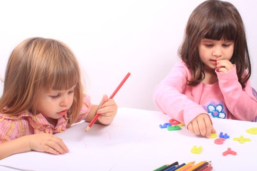 Two little preschool girls, one drawing with pencil the other playing with letters