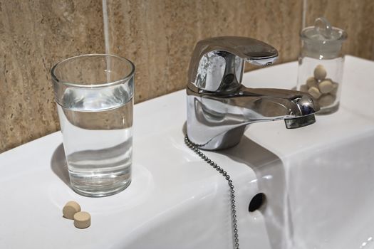 Glass of water and pile of blister packs in bathroom shelf