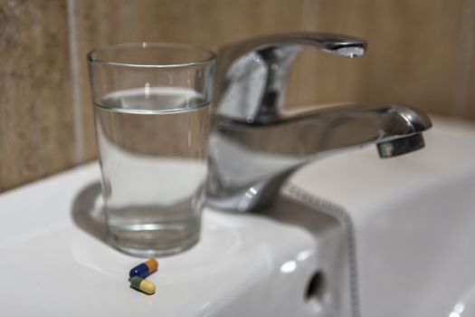 Glass of water and pile of blister packs in bathroom shelf