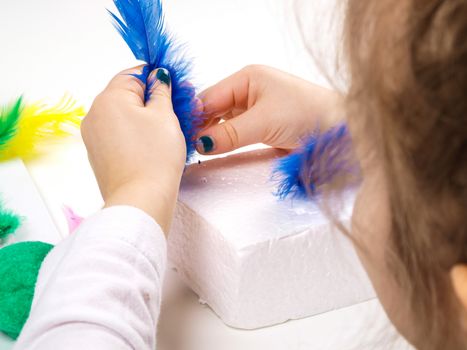 Little girls hands playing with colorful feathers, creating Easter decoration