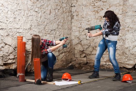 Two young long-haired woman works to repair an old house with an electric drill and cordless screwdriver