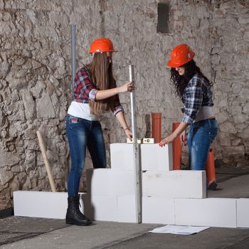 Two young long-haired woman repairing the old house and build a new wall from blocks in accordance with drawing