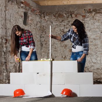 Two young long-haired woman repairing the old house and build a new wall from blocks in accordance with drawing