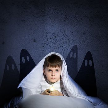 image of a boy under the covers with a flashlight the night afraid of ghosts