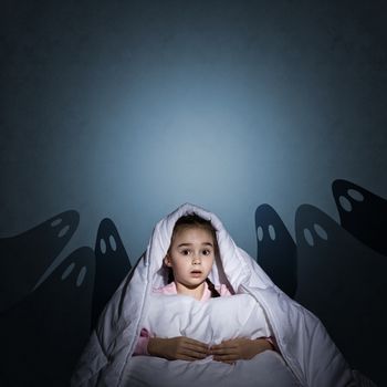 image of a girl under the covers with a flashlight the night afraid of ghosts