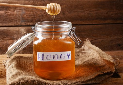 Fresh honey in glass jar on wooden background