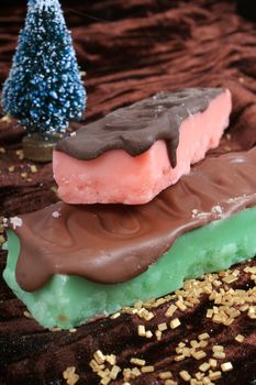 Strawberry pink, and mint green fudge bars covered in chocolate with gold flakes and christmas tree in the background