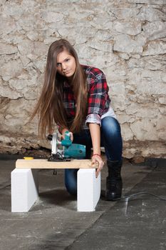 Young long-haired woman with a circular saw cuts wood at repair of an old house