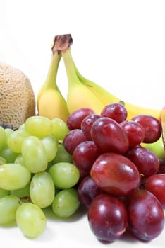 Colorful fresh fruits like grapes, cantaloupe,and bananas on a white background
