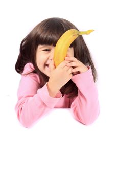 Young little girl hiding her face with a healthy banana while smiling