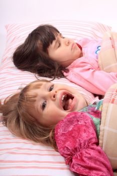 Sleepy little girls just waking up in bed, one still sleeps