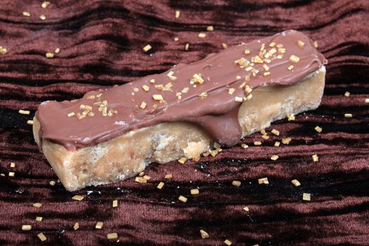 Maple or butterscotch fudge covered in chocolate on a brown velvet background with gold flakes