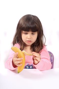 Young little girl pealing a healthy banana