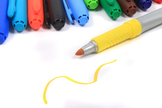 Colorful rainbow markers in blue, green,  and reds on a white background with yellow scribble and pen in the foreground