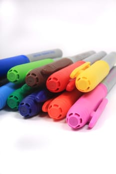 Colorful rainbow markers piled up  in blue, green, yellow and reds on a white background