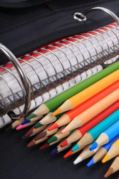 Colorful sharpened  pencil crayons for school  beside  three ring binder 