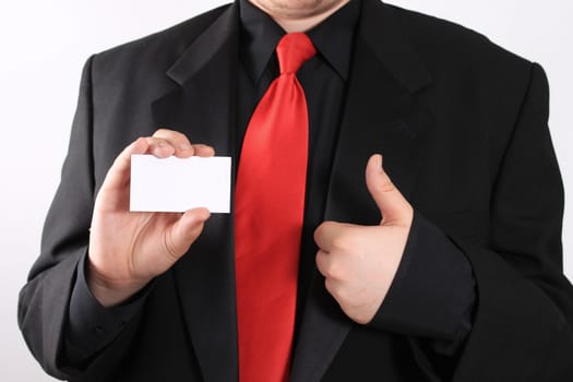 Businessman holding a blank business card in one hand and making a thumbs uup with the other on a white background (focus on card)
